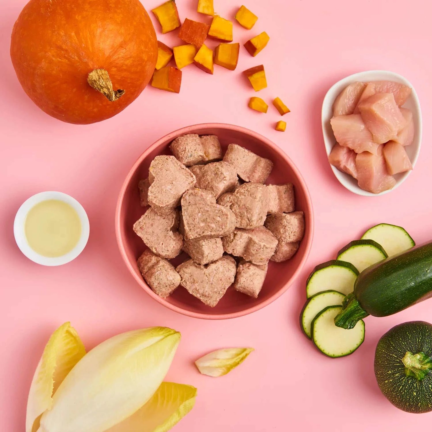 All-in-One Herzchen Huhn 750 g Beutel mit Hühnerfleisch, Kürbis, Zucchini in einem Napf auf pinkem Hintergrund, umgeben von frischen Zutaten.
