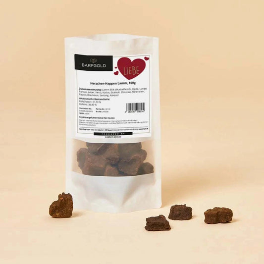 Getrocknete Herzchen-Happen aus Lammfleisch in weißer Verpackung mit roten Herz-Design, gesunder Snack für Hunde. Platziert mit einzelnen Herzchen-Happen vor dem Produkt.