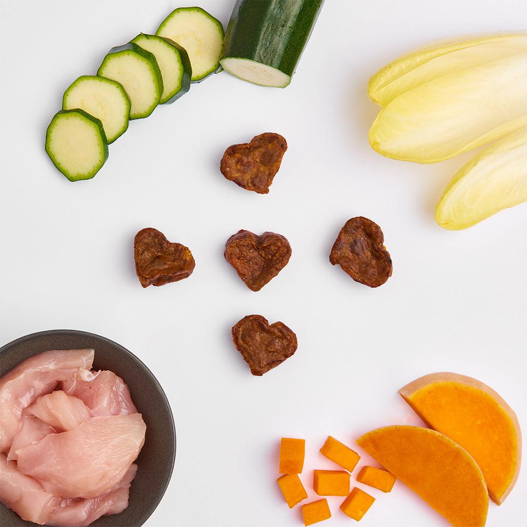 Herzchen-Happen aus getrocknetem Lammfleisch, Gemüse und Obst. Platziert mit Hühnerbrust, Karotten, Orangen und Auberginen um die Herzchen-Happen.