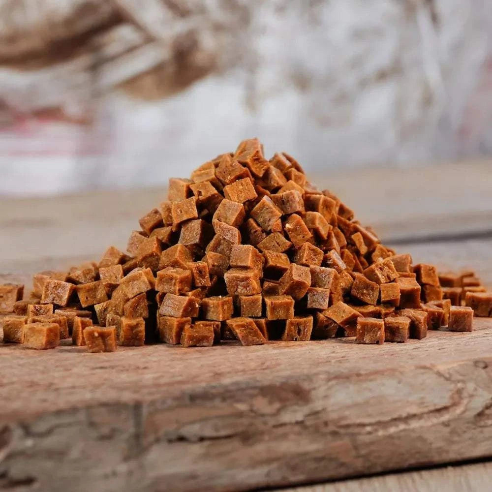 Goodies Hühnchenfleischwürfel auf Holzbrett, ideales Hundetraining, leicht portionierbar.