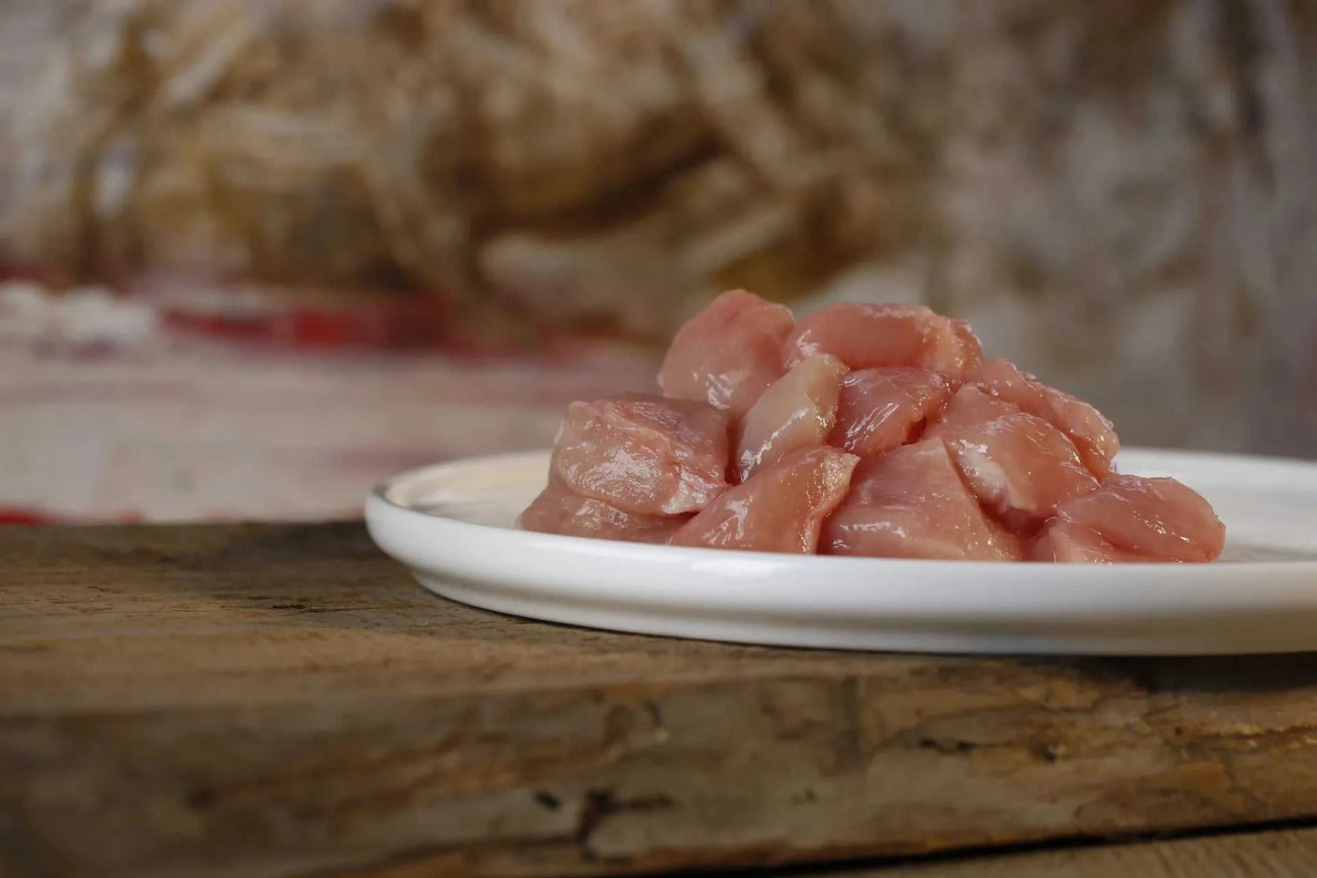 Mageres Hühnermuskelfleisch auf weißem Teller, BARF-geeignet, platziert auf einem Holzbrett.