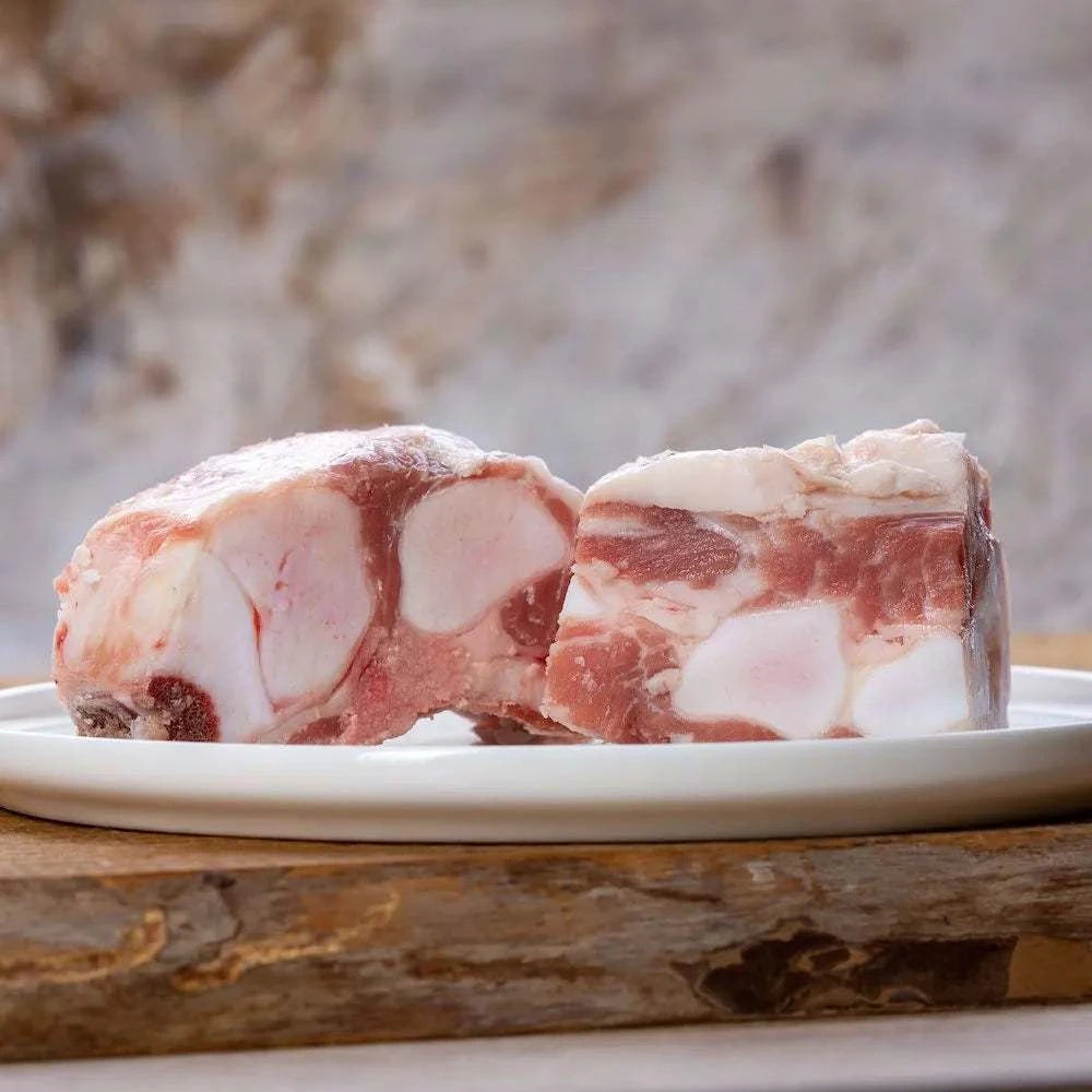 Kalbsbrustbeinknochen in Stücken auf einem Teller, ideal für Hunde, mit Fleisch und Knorpel, platziert auf einem Holzbrett.