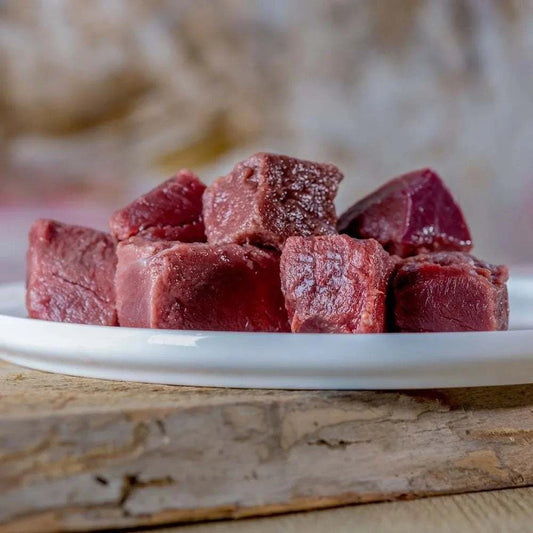 Rinderherz auf weißem Teller, rotes Muskelfleisch, nahrhaftes BARF-Futter für Hunde, enthält L-Carnitin.