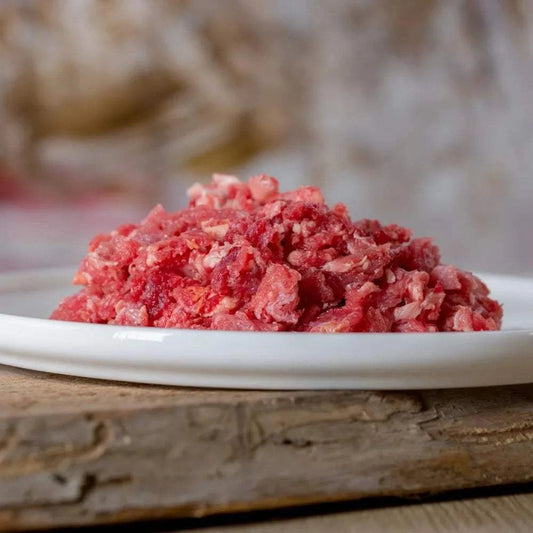 Rindermuskelfleisch grob gewolft auf weißem Teller, ideal für BARF-Ernährung von Hunden.