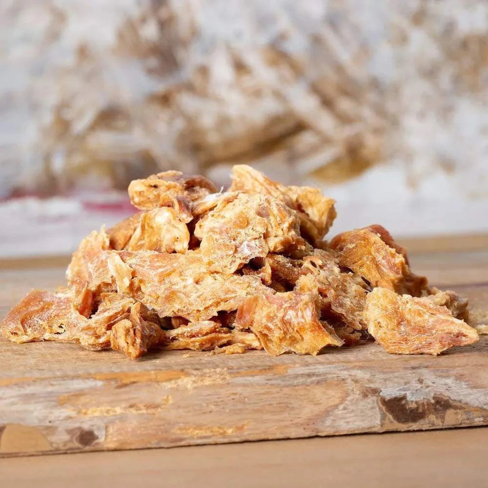 Getrocknete Hühnchenbrustfiletstücke auf Holzbrett, ideal als Snack für Hunde und Katzen.