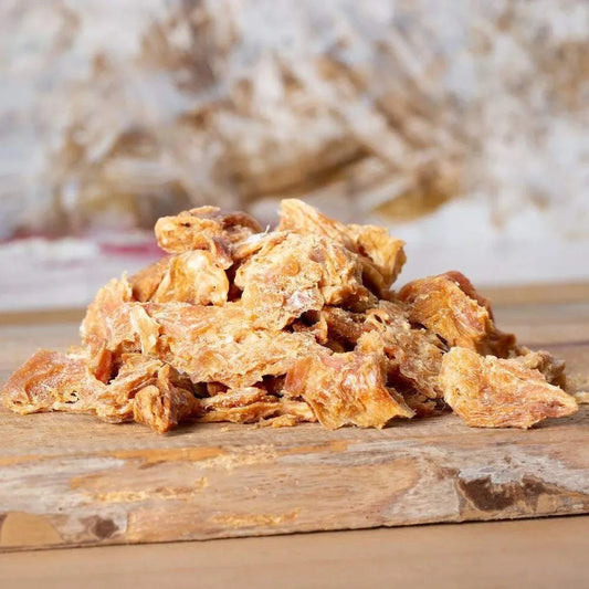 Getrocknete Hühnchenbrustfiletstücke auf Holzbrett, ideal als Snack für Hunde und Katzen.