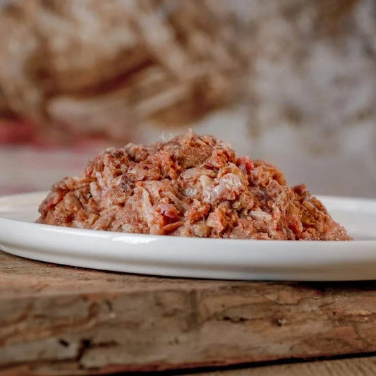 BARF-Wellnessmenü aus Hühnerhälsen, Hühnchenfleisch, Pferdeherzen, grünem Pansen und Lachs auf weißem Teller.
