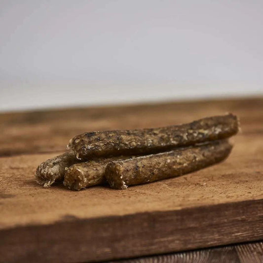 Knusperstange Elch für Hunde, ca. 13 cm lang, mit Karotte, Petersilie und Seetang, platziert auf einem Holzbrett.