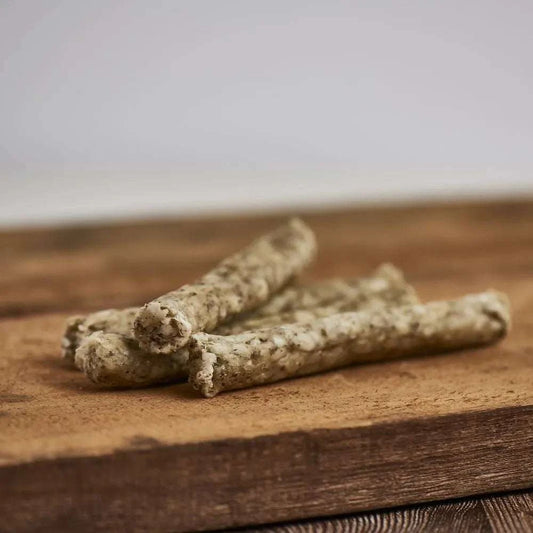 Knusperstange Rind 3er Pack für Hunde aus Rinderhaut mit Karotte, Petersilie und Seetang, platziert auf einem Holzbrett.