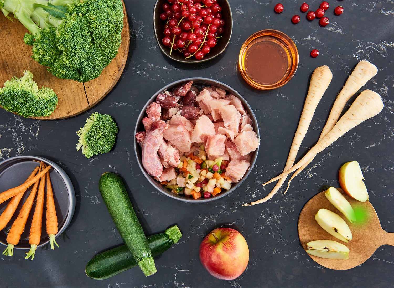 Futternapf mit Hühner-Fleisch steht auf Tisch. Auf diesem liegen viele Zutaten verteilt.