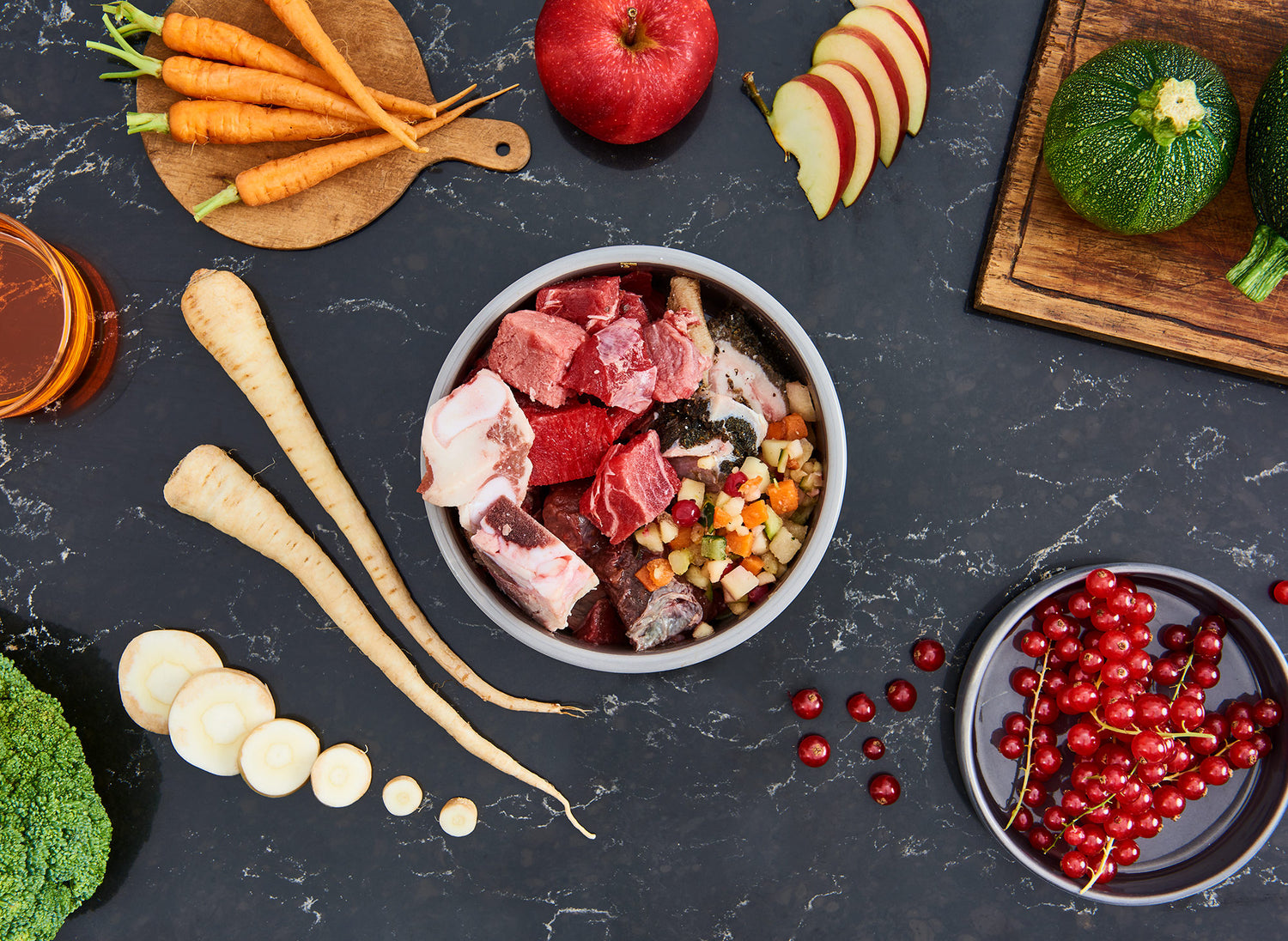 Futternapf mit Rind-Fleisch steht auf Tisch. Auf diesem liegen viele Zutaten verteilt.